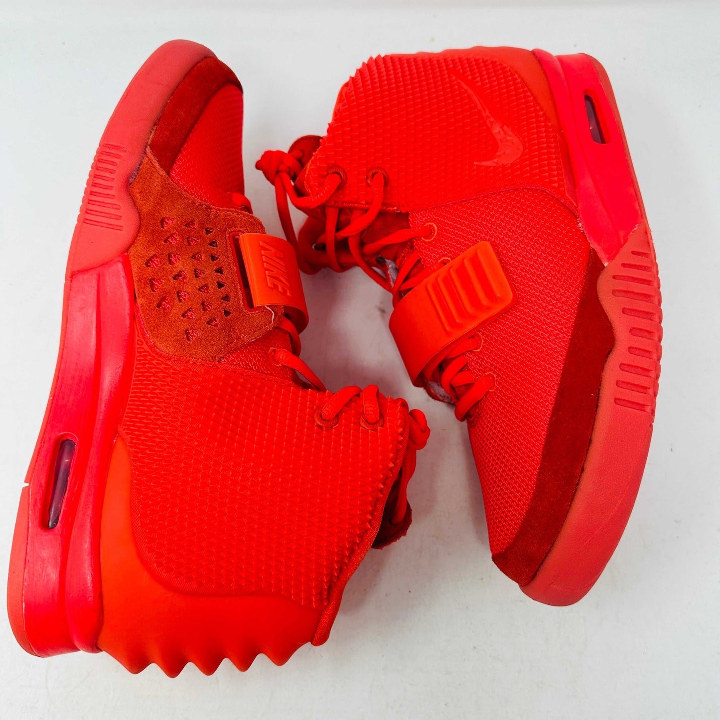 A pair of Nike Air Yeezy 2 Red October high-top sneakers, 100% authentic and brand new, features laces, a midfoot strap, and textured side detailing. Seen from the front against a white background, these bright red shoes showcase their unique style.