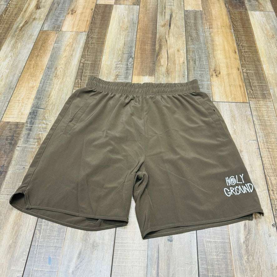 The Holy Ground Athletic Shorts (S24) feature a green design with Holy Ground printed in white on the lower left front, displayed on a wooden floor of brown and tan planks.