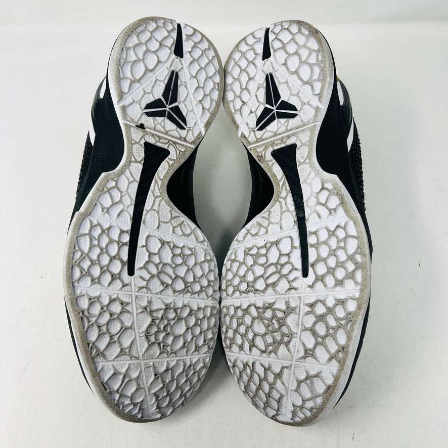The KOBE Nike Kobe 6 Protro Mambacita Sweet 16 shoe, featuring clean black and white uppers, a white Swoosh, and a small gold 2 on the heel, is displayed on top of its black box with a Nike label. A sealed bag containing black laces accompanies the box for an authentic presentation.