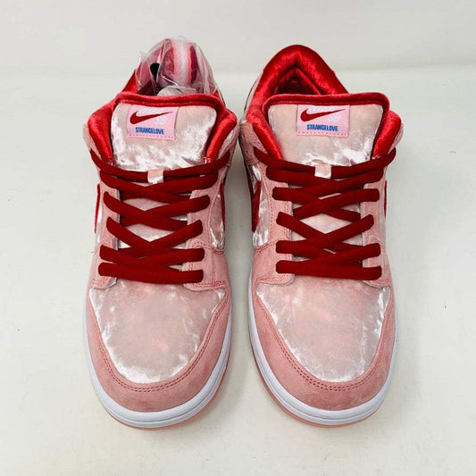 The Nike SB Dunk Low StrangeLove Skateboards, with vibrant pink and red, features a bold red swoosh, matching laces, and cartoon heart graphics on the heel. Displayed on a teal box with extra laces included, their design stands out against a plain white backdrop.
