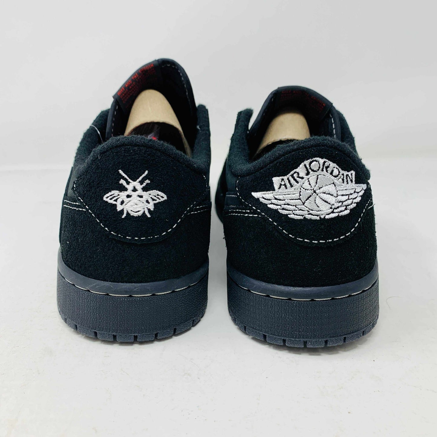 The Jordan 1 Low Travis Phantom sneakers, in black with white stitching, rest on a matching box. Authenticity shines through their design, enhanced by red inserts and the boxs subtle features.
