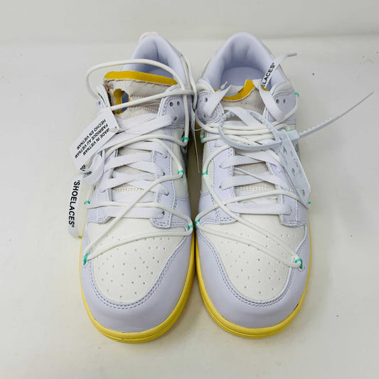 The Nike Dunk Low Off White Lot 1 sneaker, white with a metallic silver swoosh and vibrant accents, rests on a brown shoebox. Its unique lace design and 01 of 50 detailing highlight its 2021 release against a plain white backdrop.