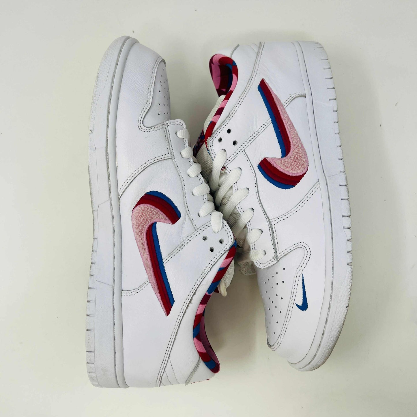 A white Nike SB Dunk Low Parra from 2019 with a multicolored swoosh rests on a black and teal box. The authentic shoes feature clean uppers, size 10.5, as indicated on the label.