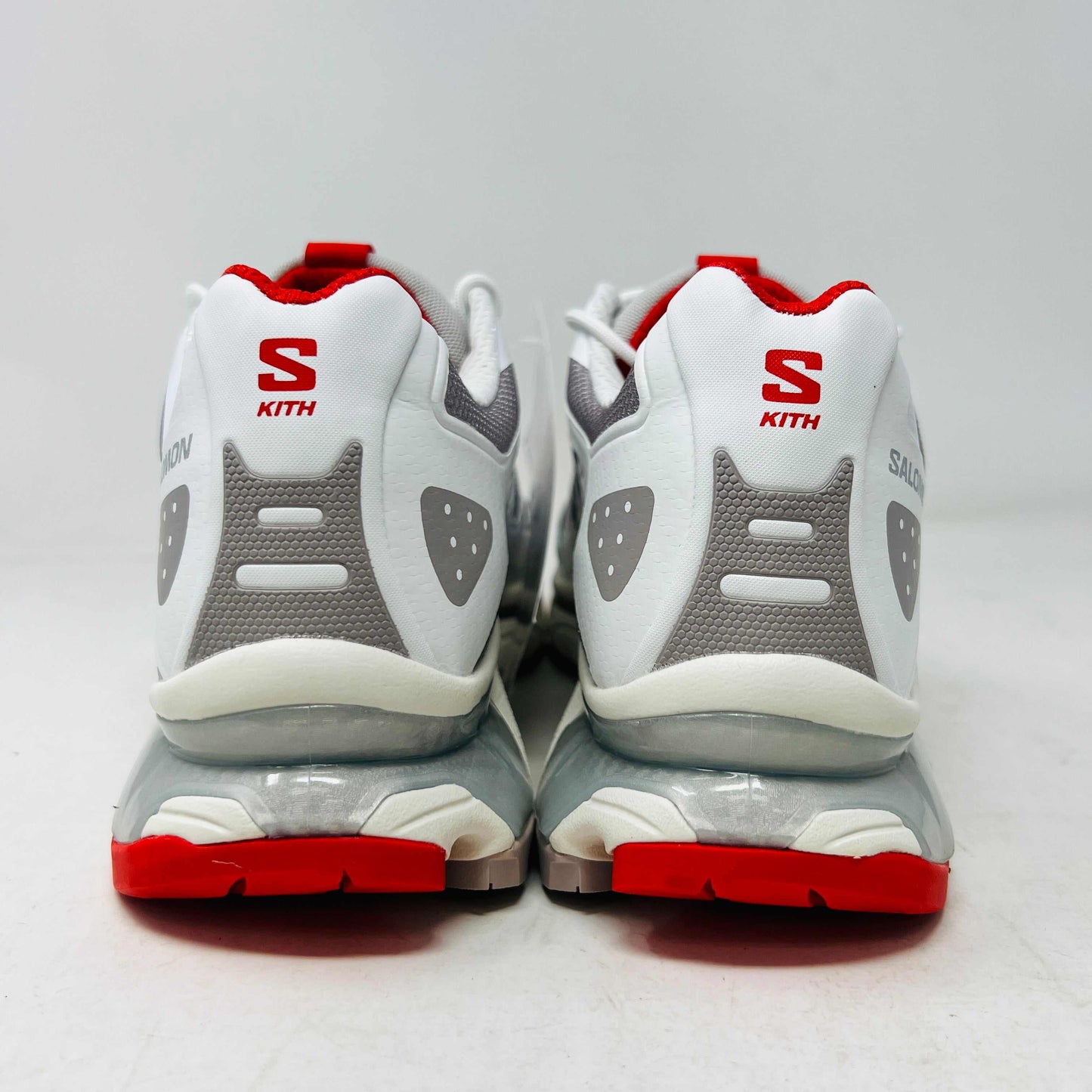 The Salomon XT-4K Kith Kithmas White Red sneakers rest on a black Kith box, with an extra laces bag. The shoes are 100% authentic, showcasing red accents and branding details.