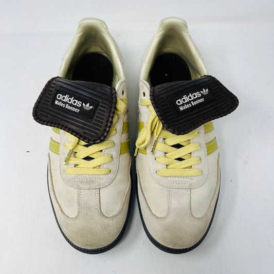 The 2023 adidas Samba Wales Bonner Ecrtin Brown sneakers feature beige uppers with three yellow stripes, a brown logo flap, and black soles. Despite general wear, the side and tongue branding stays distinct. Theyre displayed side by side on a white background.