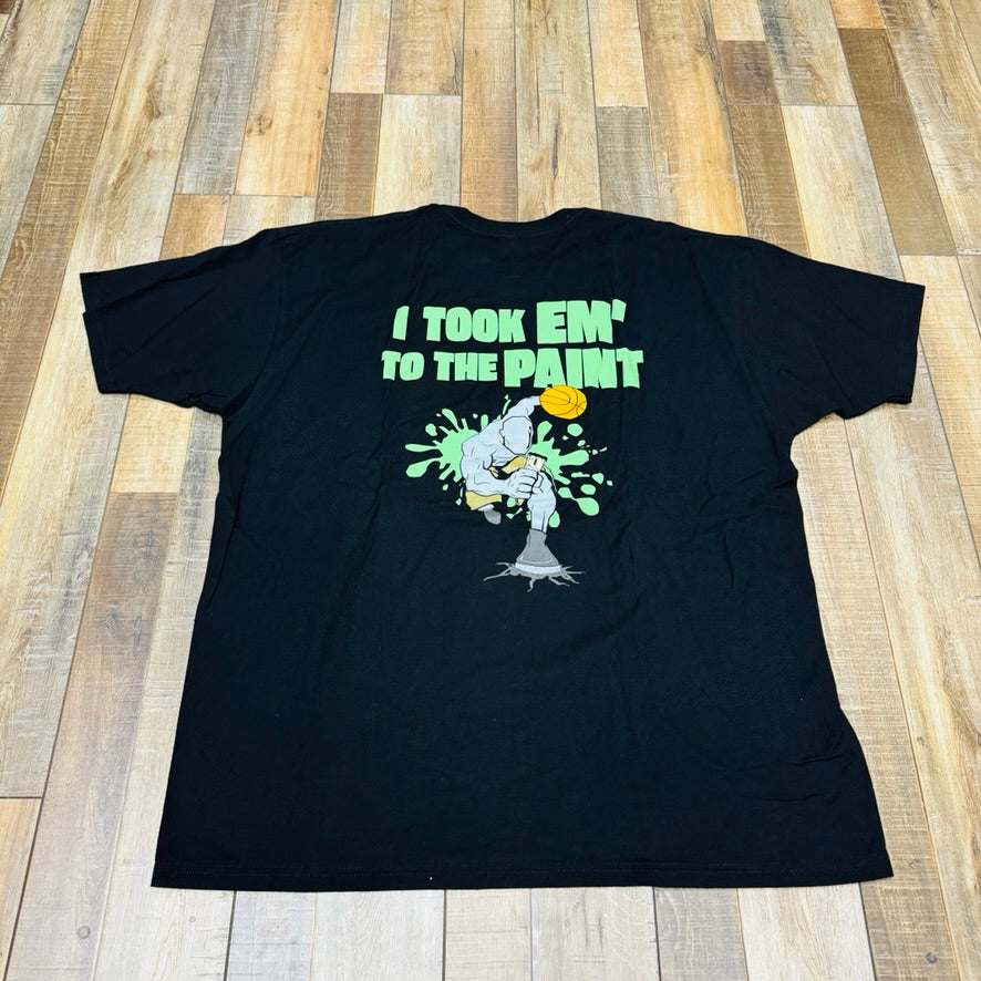 Holy Ground HG And-1 Tee in black, featuring a small white chest logo, is laid flat on a wooden floor.