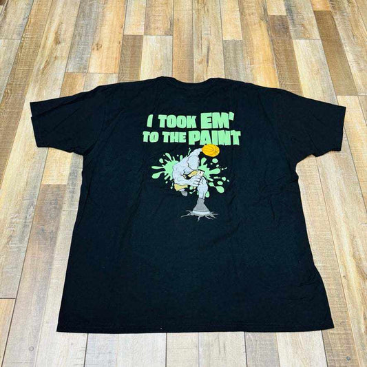 Holy Ground HG And-1 Tee in black, featuring a small white chest logo, is laid flat on a wooden floor.