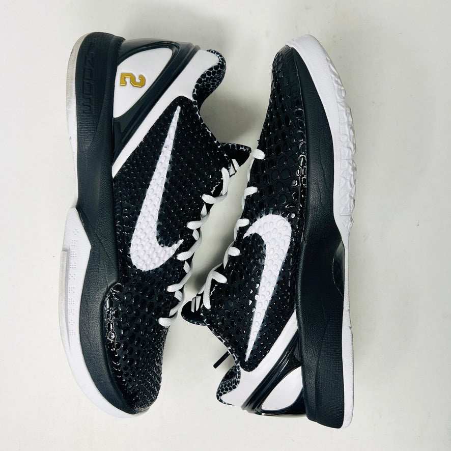 The KOBE Nike Kobe 6 Protro Mambacita Sweet 16 shoe, featuring clean black and white uppers, a white Swoosh, and a small gold 2 on the heel, is displayed on top of its black box with a Nike label. A sealed bag containing black laces accompanies the box for an authentic presentation.