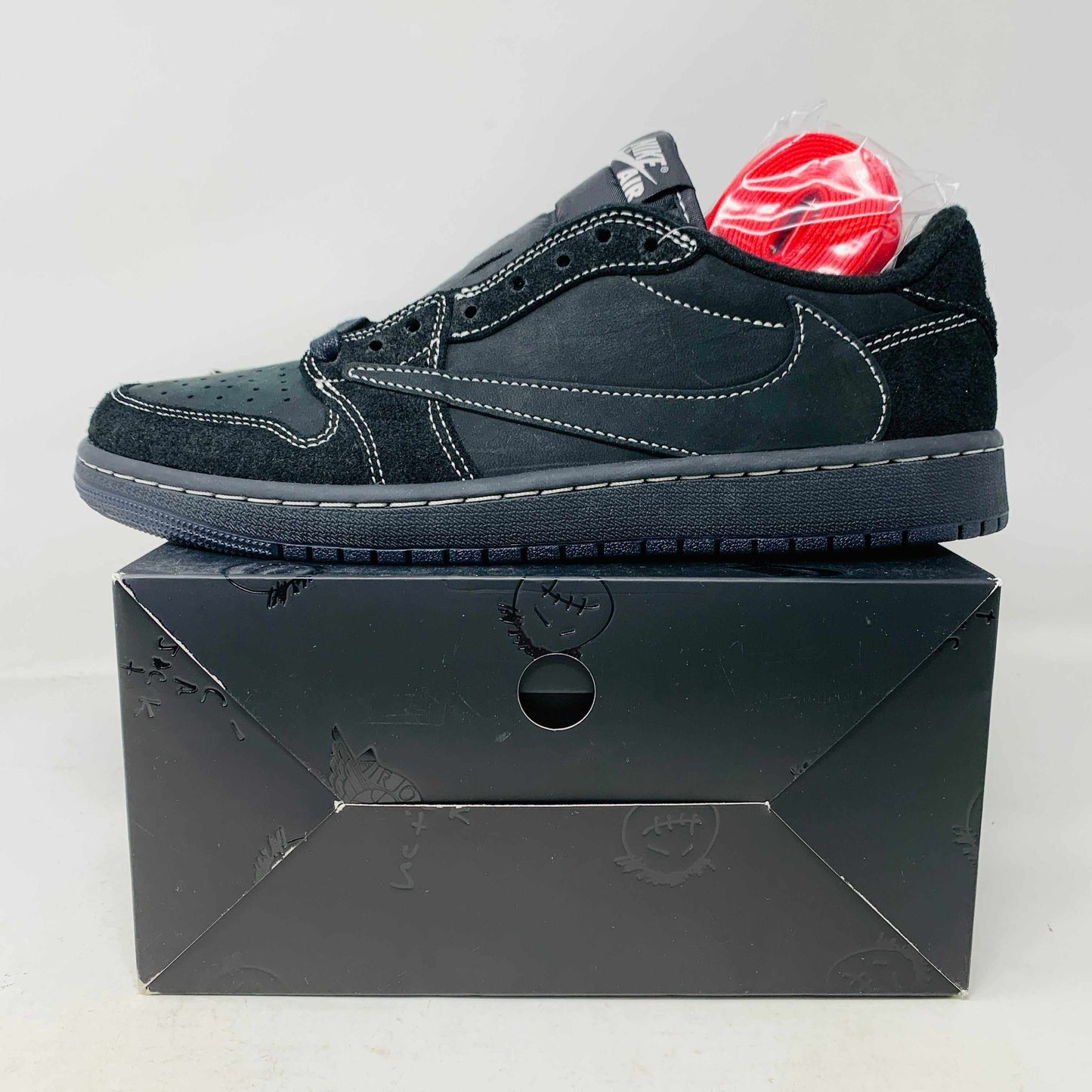 Jordan 1 Low Travis Phantom on box with red and black laces, side view.