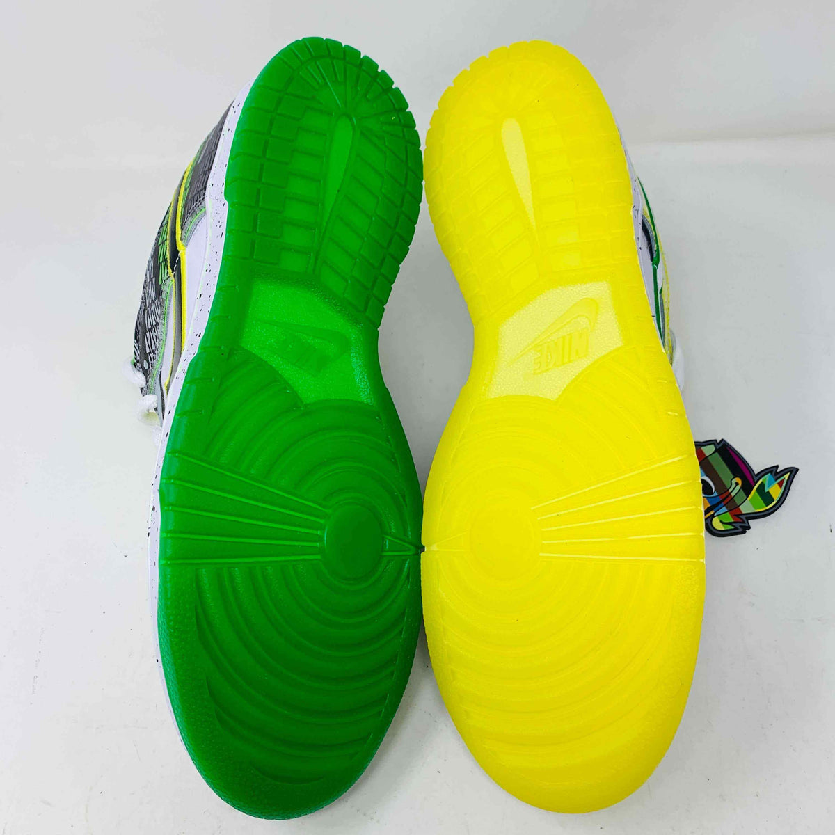 The Nike Dunk Low What the Duck Away University of Oregon PE is a vibrant sneaker featuring green, white, and black patterns with a black Nike swoosh outlined in yellow. It includes white laces, extra laces, a speckled white midsole, and a padded yellow lining atop a bright green shoebox. 100% authentic.