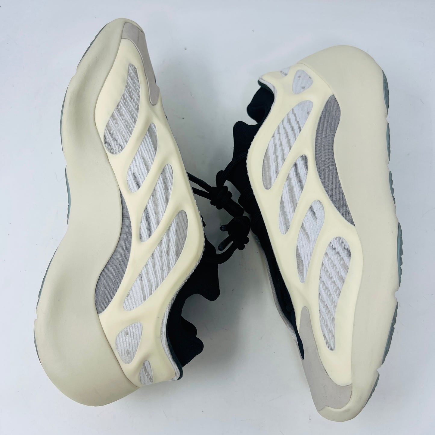 The adidas Yeezy 700 V3 Azael features a futuristic design with a black mesh upper, white and beige sculpted overlays, and an intricate lacing system. It has a sleek, modern look set against a plain white background, showing minimal wear for that fresh out-of-the-box condition.