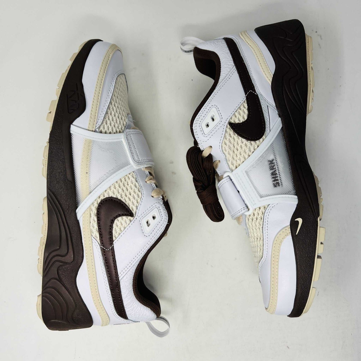 The Nike Zoom Field Jaxx Travis Scott Light Chocolate sneaker showcases a white and brown design with mesh and leather textures, Velcro strap, brown laces, and a prominent brown swoosh. It sits on a blue Nike shoebox.