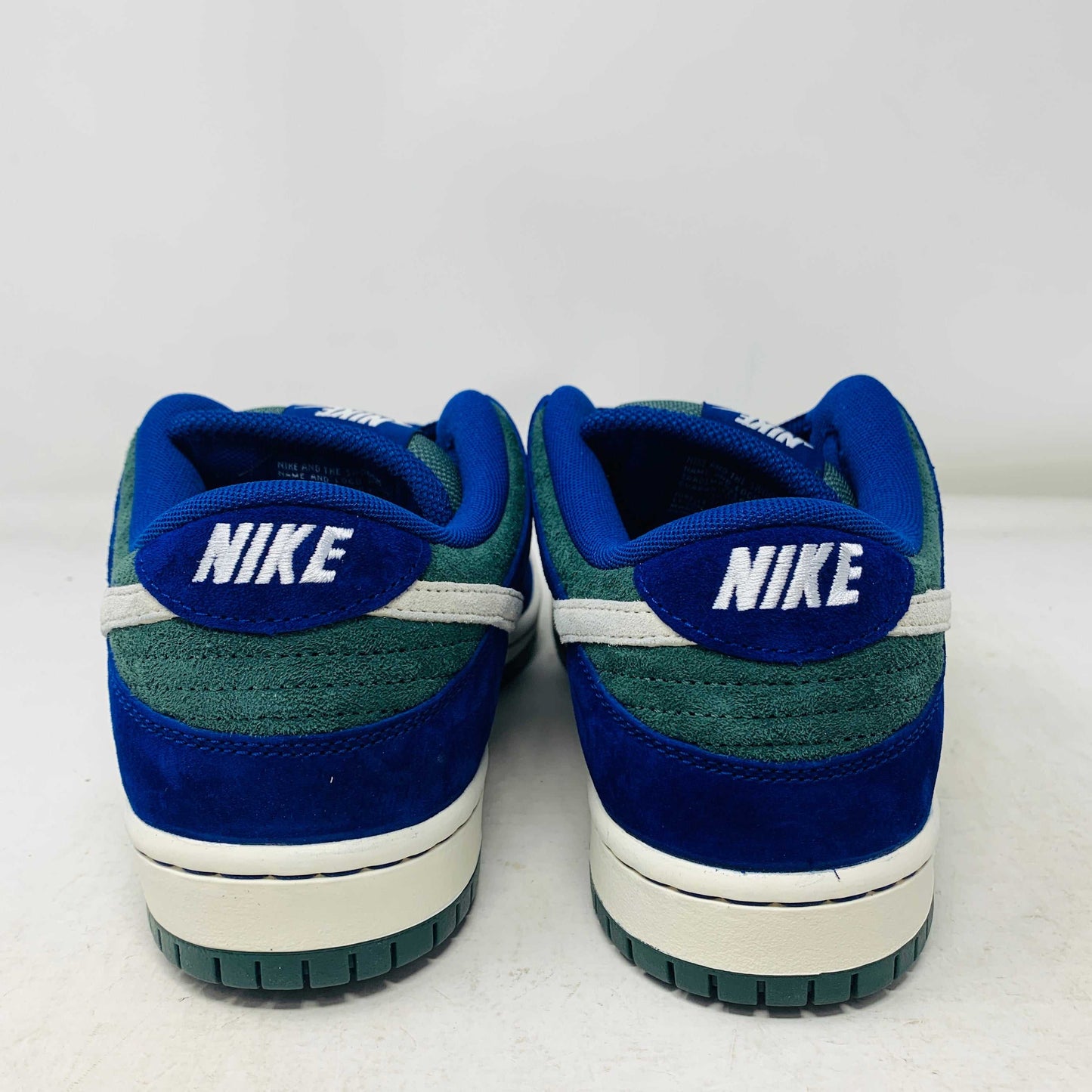 The Nike SB Dunk Low Deep Royal Blue sneaker, featuring a sleek blue and green design with a white swoosh, sits atop a purple Nike box. A bonus set of green laces accompanies the shoe, perfect for updating your style in 2024.