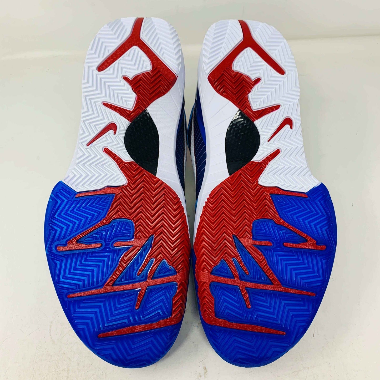 The image displays the soles of Nike Kobe 4 Protro Philly (2024) basketball shoes, featuring a vivid red, white, and blue pattern that captures Philadelphias essence. Zigzag grooves offer excellent traction, enhanced by unique logo designs.