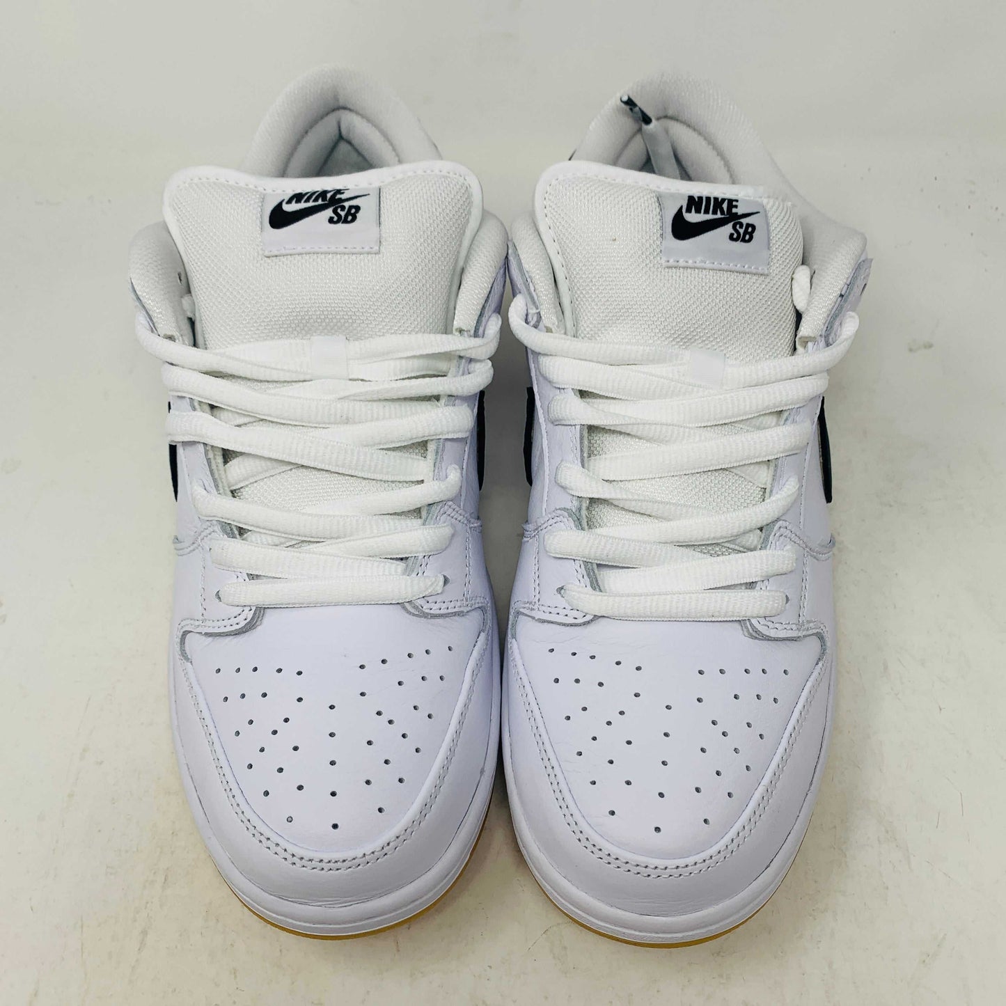 A brand new Nike SB Dunk Low in white with a black swoosh, white laces, and a gum sole rests on a 2023 purple Nike SB shoebox featuring bold white text. The profile view showcases its authentic design.
