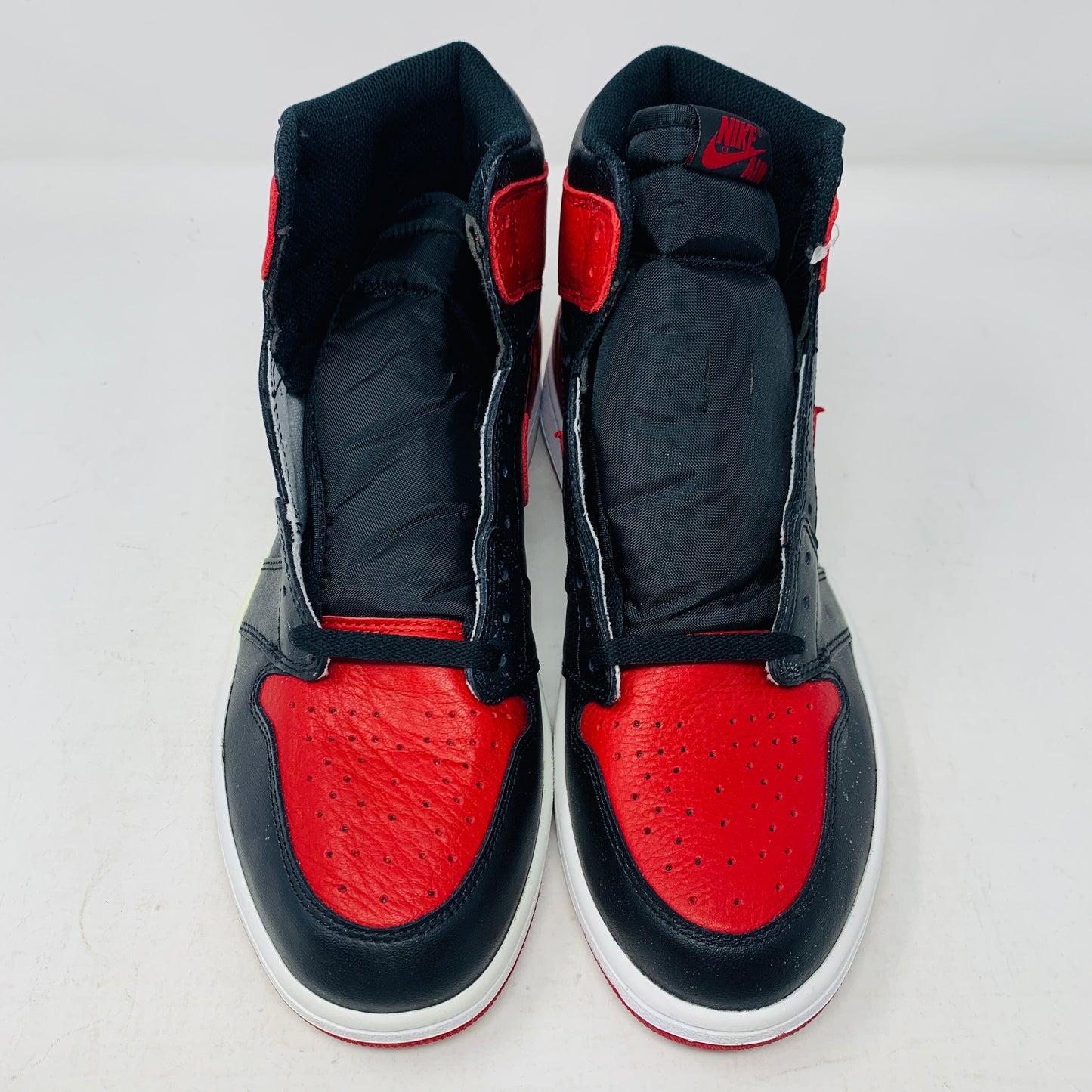 The Jordan 1 High Bred 2016 sneakers, by Jordan, are brand-new black and red high-tops with a white sole. Viewed from above, they showcase an unlaced look with a perforated design on the toe area.