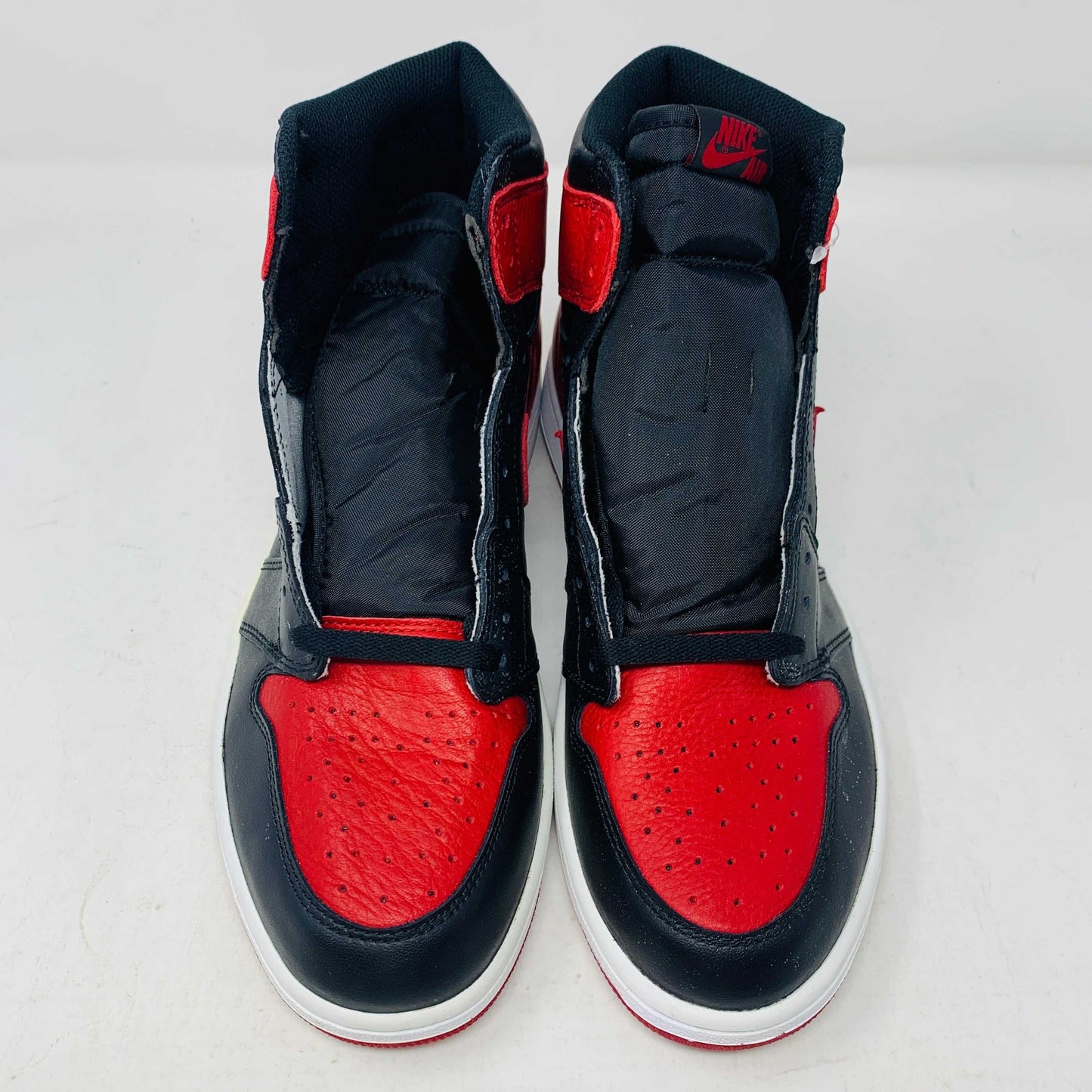 The Jordan 1 High Bred 2016 sneakers, by Jordan, are brand-new black and red high-tops with a white sole. Viewed from above, they showcase an unlaced look with a perforated design on the toe area.