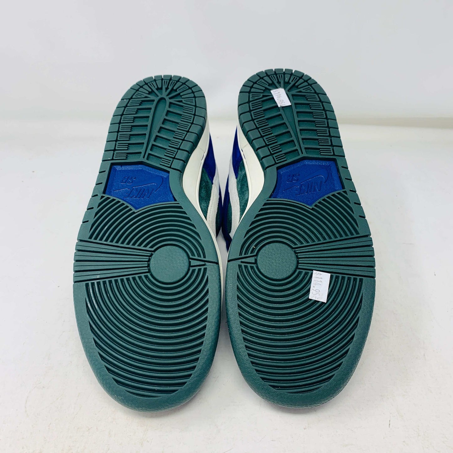 The Nike SB Dunk Low Deep Royal Blue sneaker, featuring a sleek blue and green design with a white swoosh, sits atop a purple Nike box. A bonus set of green laces accompanies the shoe, perfect for updating your style in 2024.