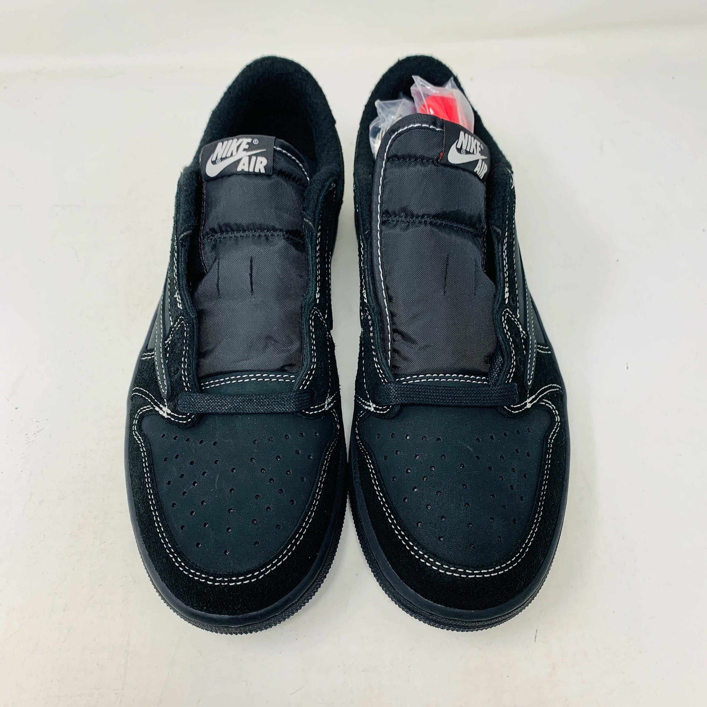 The Jordan 1 Low Travis Phantom sneakers, in black with white stitching, rest on a matching box. Authenticity shines through their design, enhanced by red inserts and the boxs subtle features.