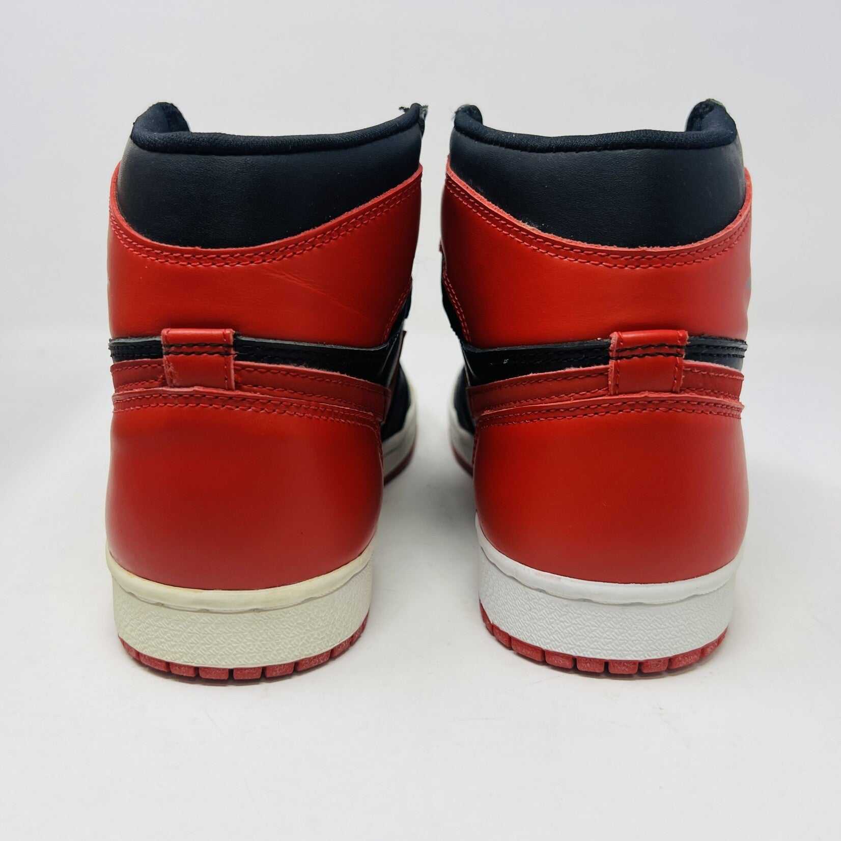 A pair of brand new Jordan 1 Retro Bred (1994) sneakers is displayed on a box, featuring the iconic Nike swoosh and wings logo. A black-and-white photo of the shoes is behind them. The box has various sneaker-related graphics, emphasizing their authenticity.