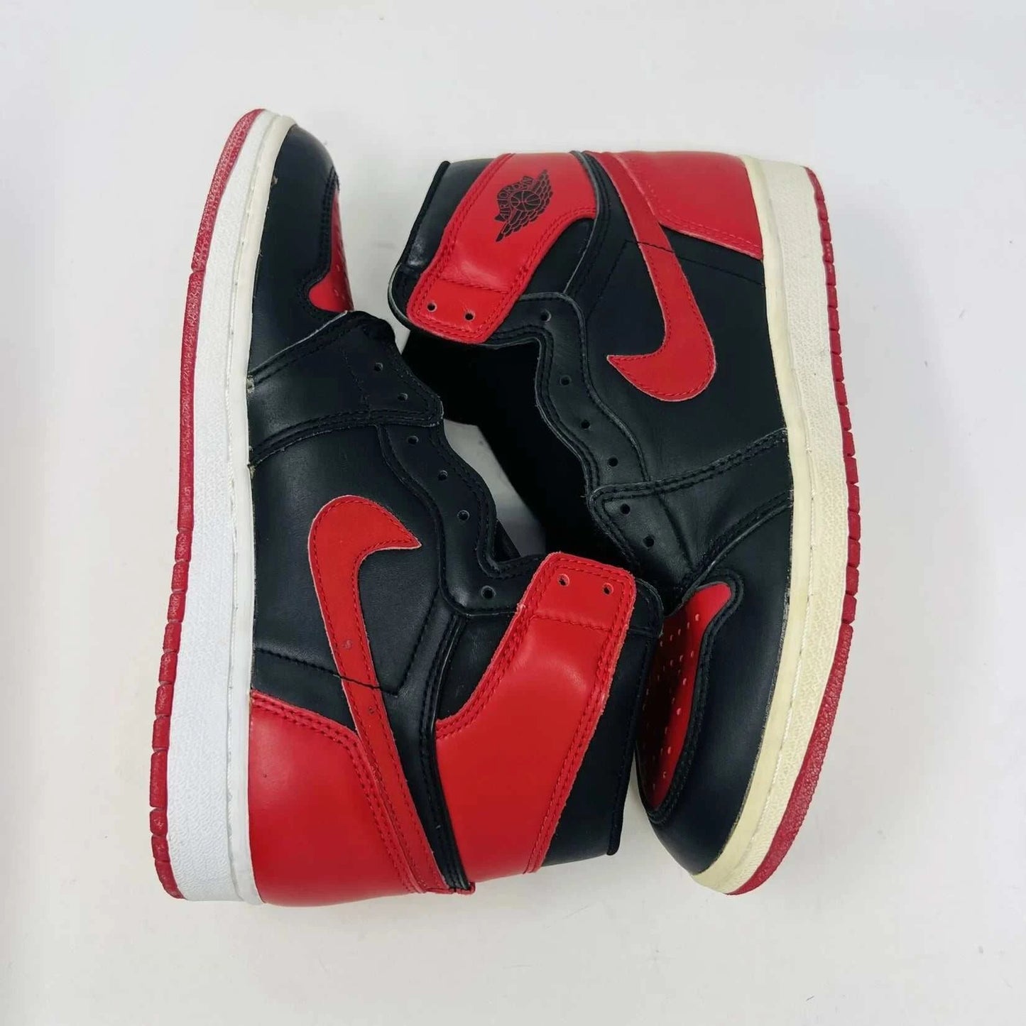 A pair of brand new Jordan 1 Retro Bred (1994) sneakers is displayed on a box, featuring the iconic Nike swoosh and wings logo. A black-and-white photo of the shoes is behind them. The box has various sneaker-related graphics, emphasizing their authenticity.
