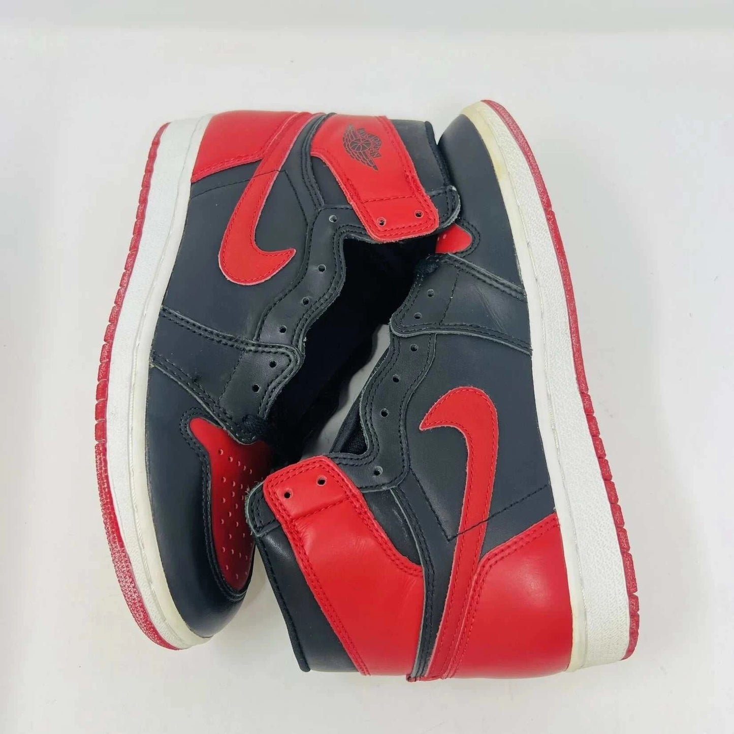 A pair of brand new Jordan 1 Retro Bred (1994) sneakers is displayed on a box, featuring the iconic Nike swoosh and wings logo. A black-and-white photo of the shoes is behind them. The box has various sneaker-related graphics, emphasizing their authenticity.