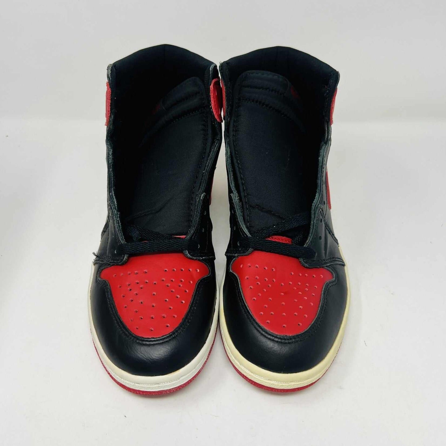 A pair of brand new Jordan 1 Retro Bred (1994) sneakers is displayed on a box, featuring the iconic Nike swoosh and wings logo. A black-and-white photo of the shoes is behind them. The box has various sneaker-related graphics, emphasizing their authenticity.