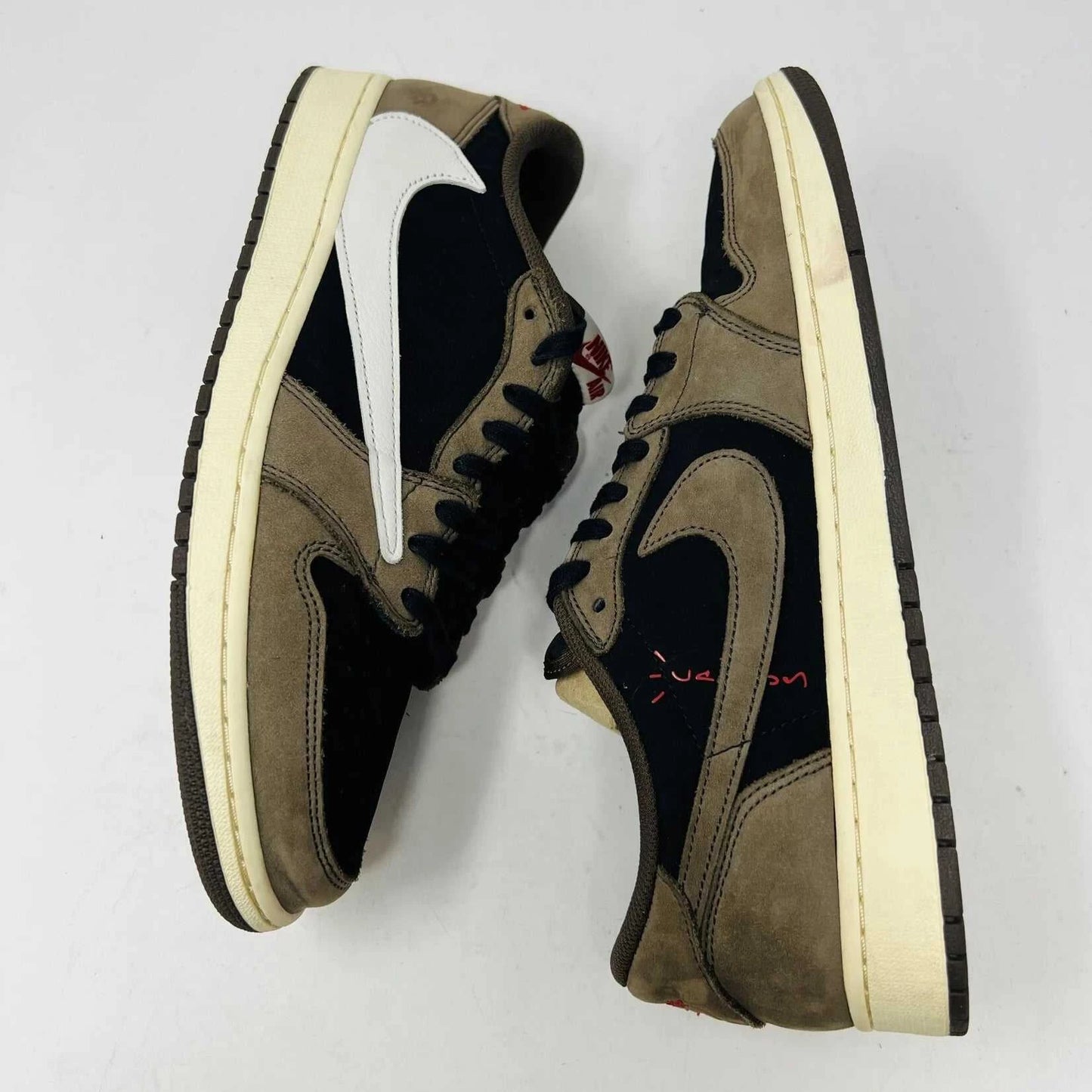 The Jordan 1 Retro Low OG SP Travis Scott Mocha sneakers, released in 2019 and featuring brown, black, and white tones, are displayed on a Nike box. Two extra lace sets, one red and one pink, are included in plastic bags beside the box.