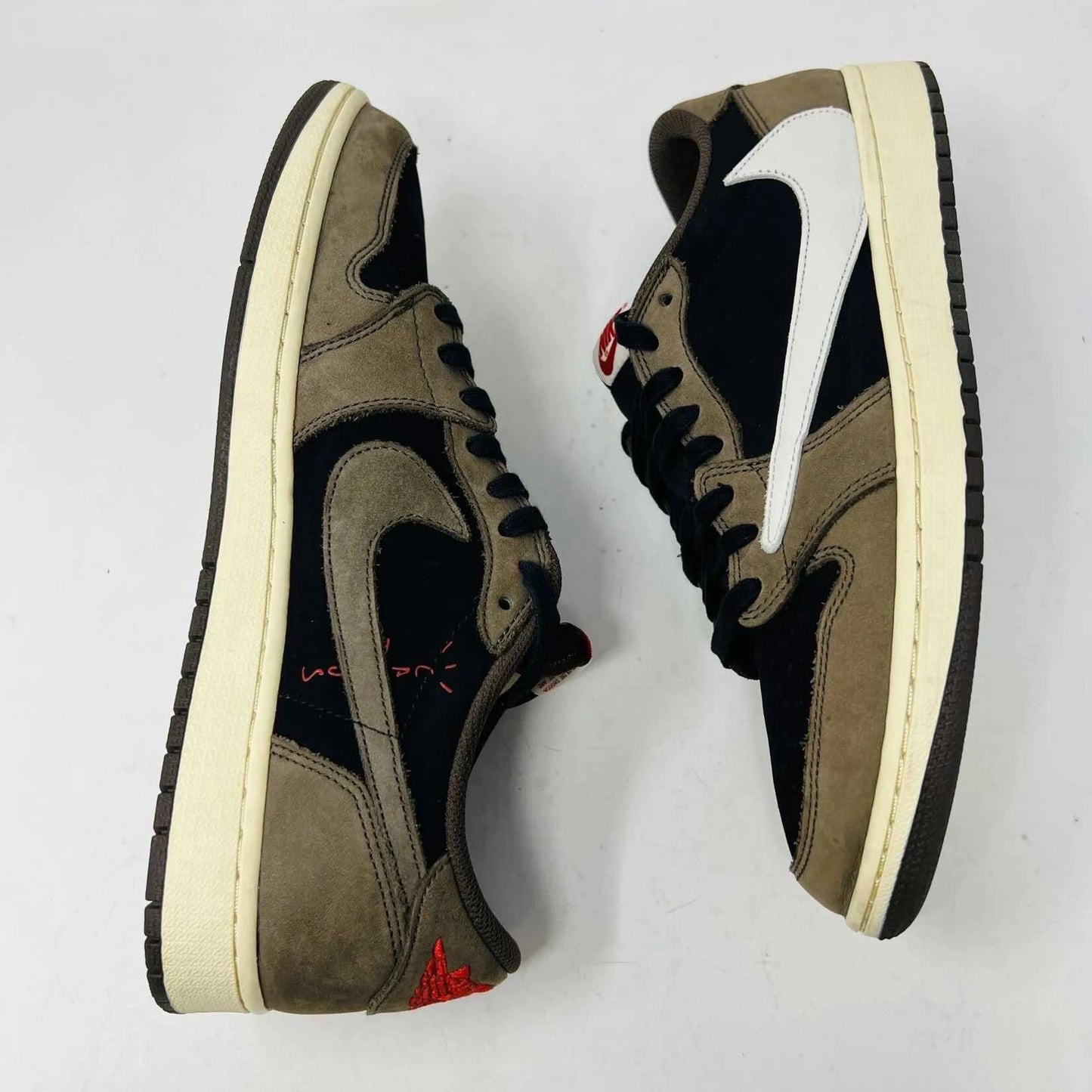 The Jordan 1 Retro Low OG SP Travis Scott Mocha sneakers, released in 2019 and featuring brown, black, and white tones, are displayed on a Nike box. Two extra lace sets, one red and one pink, are included in plastic bags beside the box.