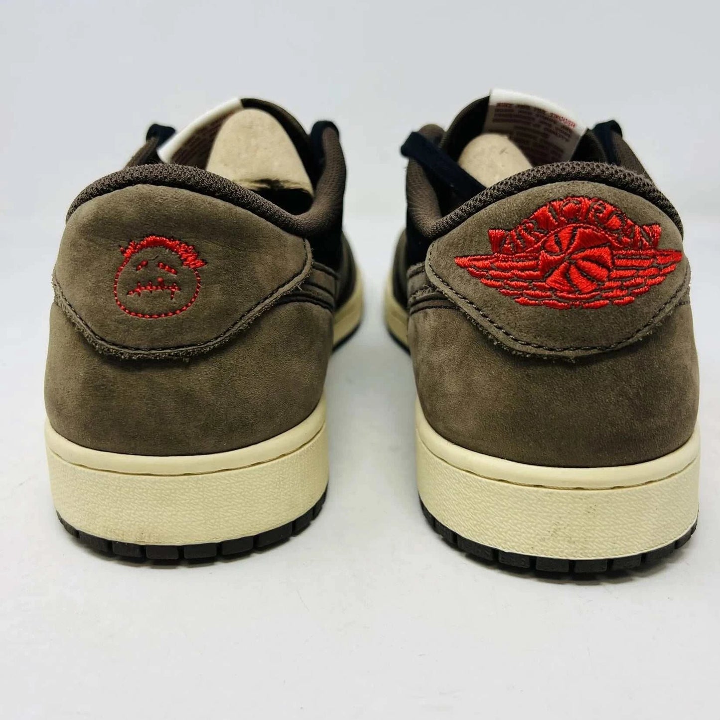 The Jordan 1 Retro Low OG SP Travis Scott Mocha sneakers, released in 2019 and featuring brown, black, and white tones, are displayed on a Nike box. Two extra lace sets, one red and one pink, are included in plastic bags beside the box.