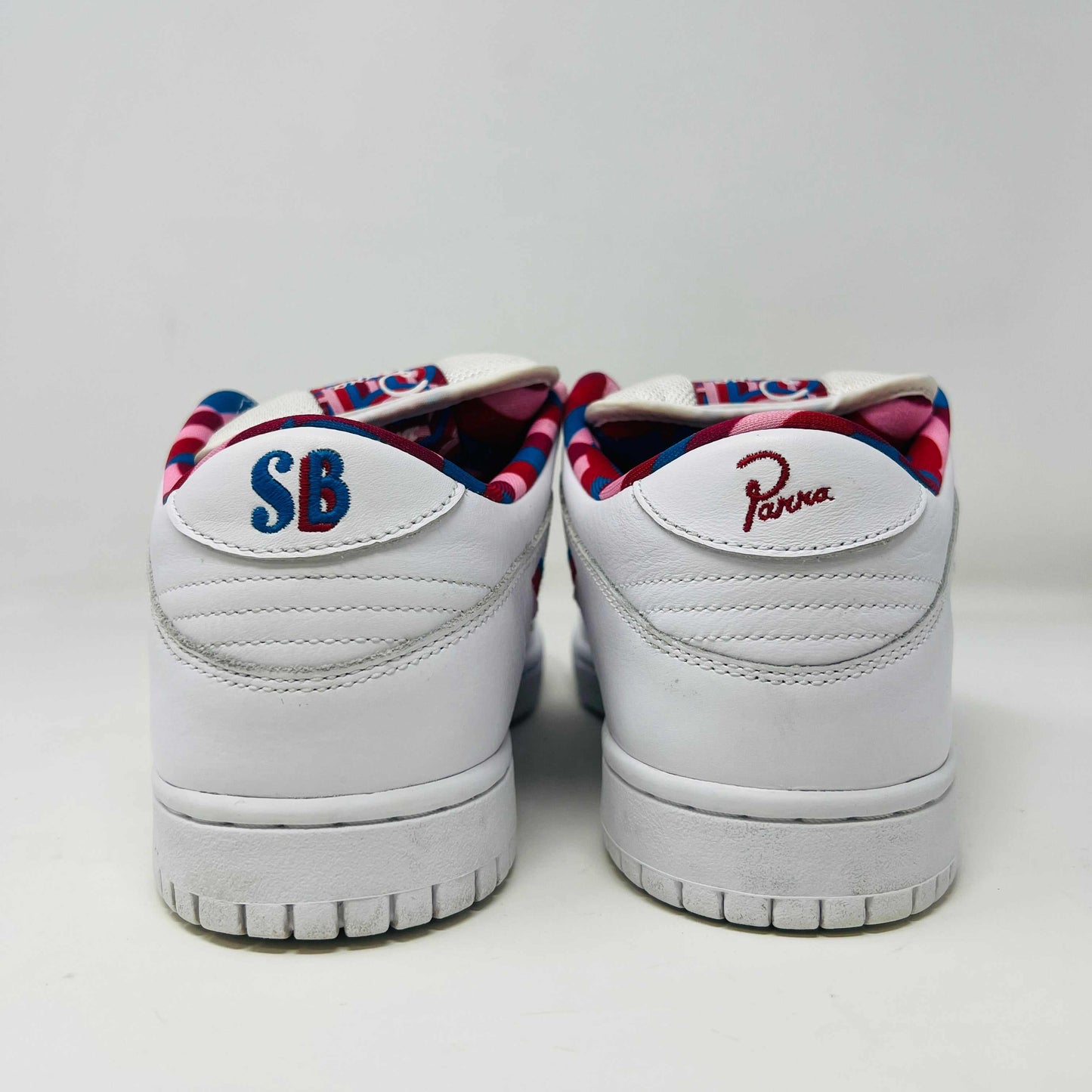 A white Nike SB Dunk Low Parra from 2019 with a multicolored swoosh rests on a black and teal box. The authentic shoes feature clean uppers, size 10.5, as indicated on the label.