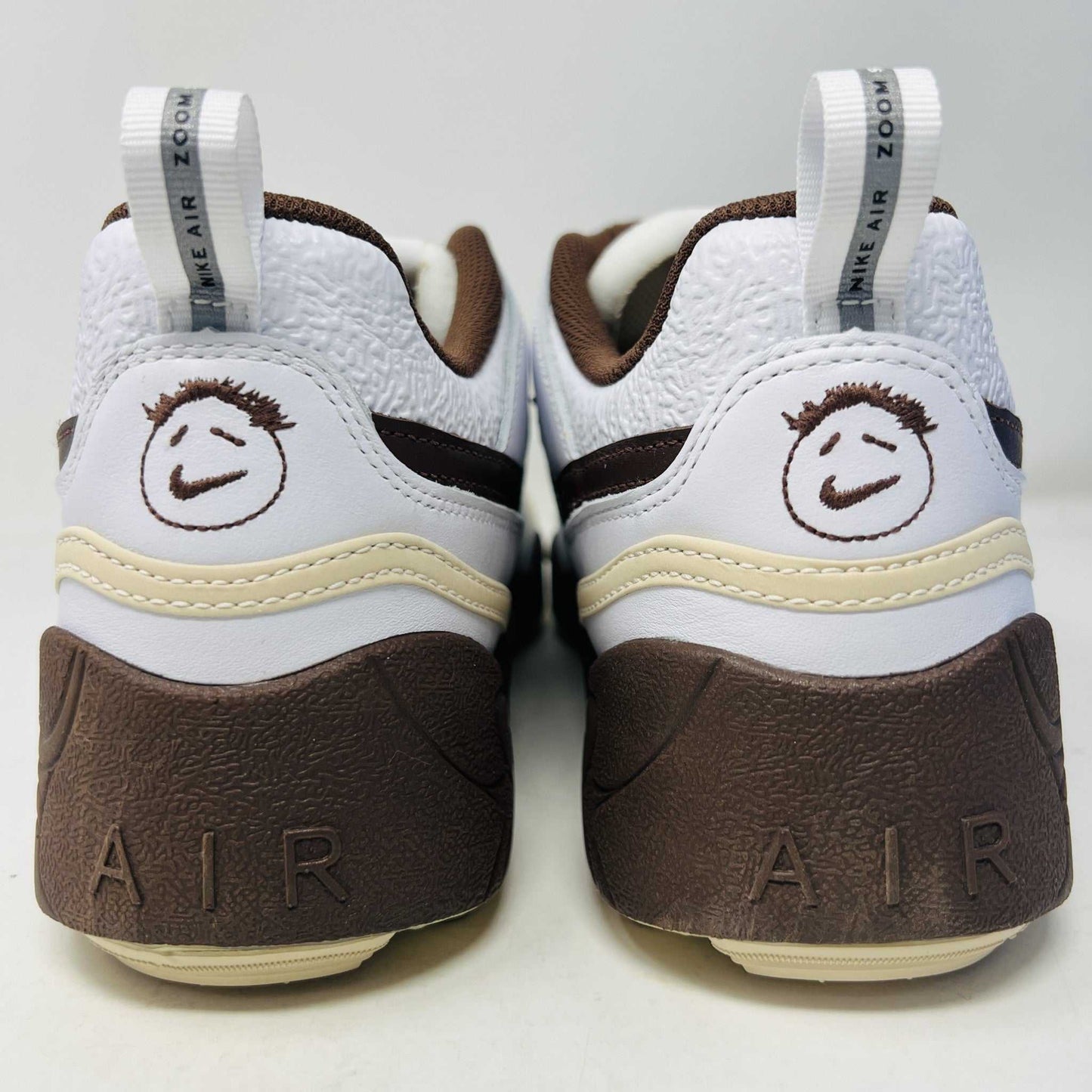 The Nike Zoom Field Jaxx Travis Scott Light Chocolate sneaker showcases a white and brown design with mesh and leather textures, Velcro strap, brown laces, and a prominent brown swoosh. It sits on a blue Nike shoebox.