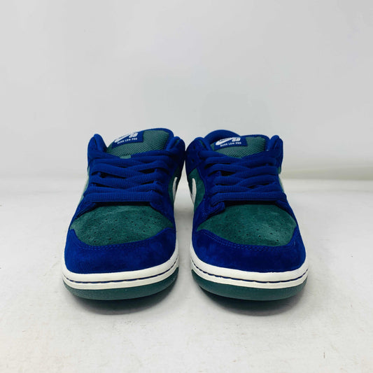 The Nike SB Dunk Low Deep Royal Blue sneaker, featuring a sleek blue and green design with a white swoosh, sits atop a purple Nike box. A bonus set of green laces accompanies the shoe, perfect for updating your style in 2024.