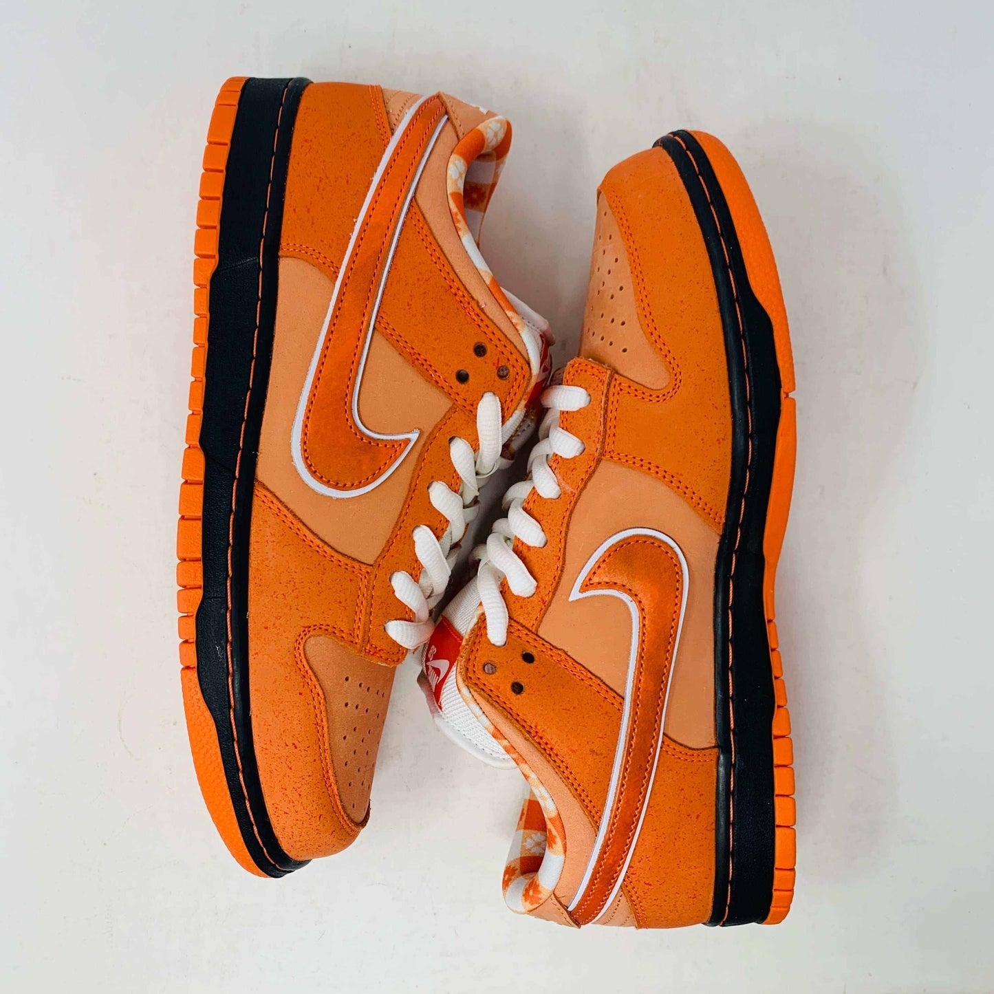 The authentic Nike SB Dunk Low Orange Lobster Concepts sneaker sits on a green and yellow Nike SB box. It features a white sole with black trim, an orange swoosh, and extra laces neatly positioned in front of the box.