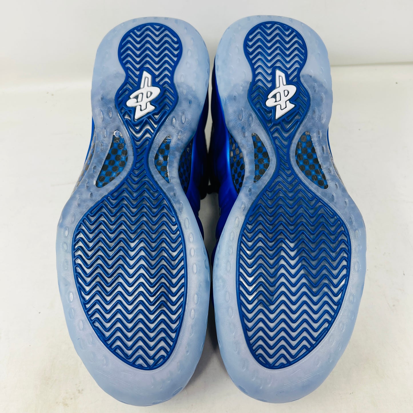 A brand-new Nike Air Foamposite One International Blue sneaker, featuring a striking blue upper with black accents, rests on a sleek black Nike shoebox. It has black mesh laces, a translucent sole with carbon fiber plate, and an iconic side swoosh.
