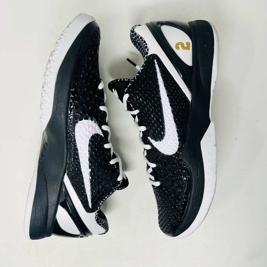 The KOBE Nike Kobe 6 Protro Mambacita Sweet 16 shoe, featuring clean black and white uppers, a white Swoosh, and a small gold 2 on the heel, is displayed on top of its black box with a Nike label. A sealed bag containing black laces accompanies the box for an authentic presentation.