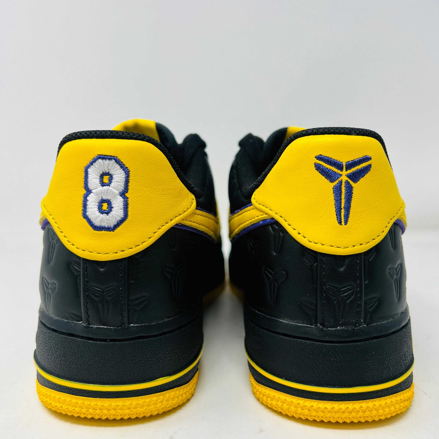 The new black Nike Air Force 1 Low Kobe Bryant Lakers Away sneakers have yellow accents like a swoosh and sole, sitting on a white box with the Nike logo and icon. These 100% authentic shoes are available as a final sale item.