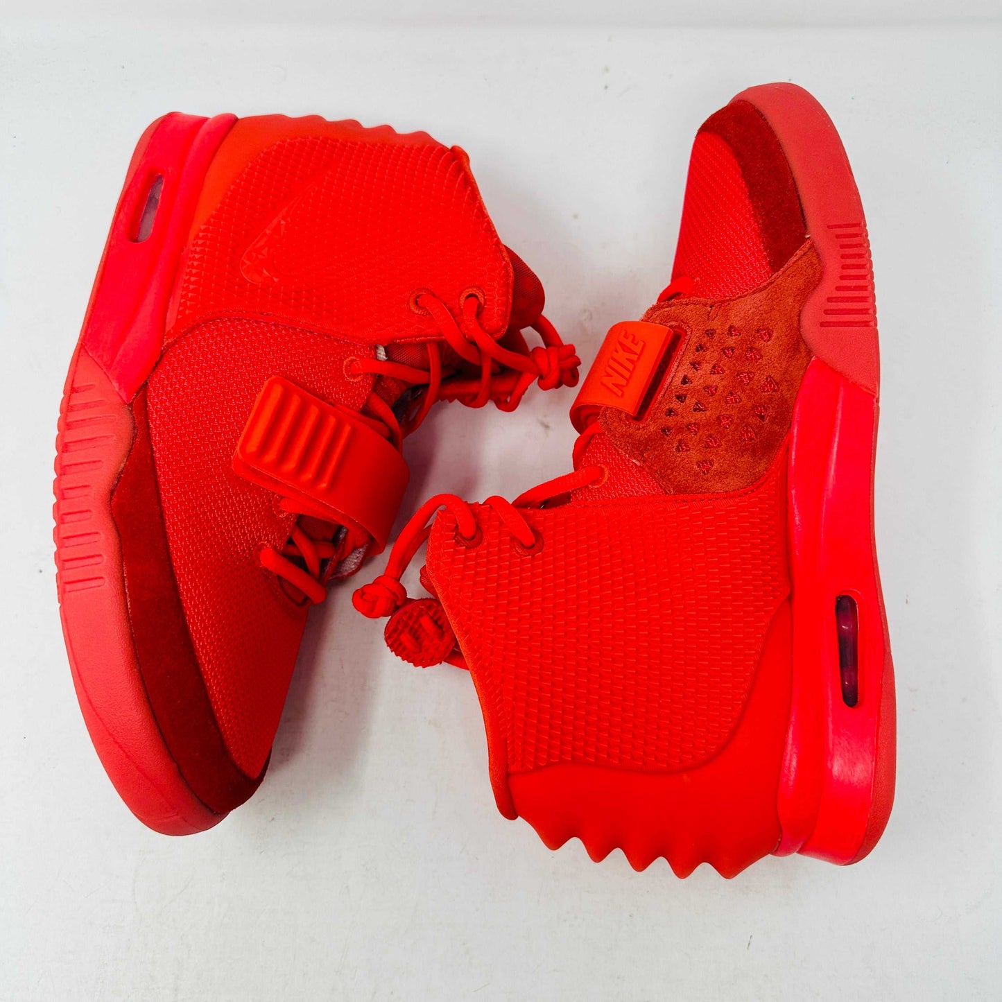 A pair of Nike Air Yeezy 2 Red October high-top sneakers, 100% authentic and brand new, features laces, a midfoot strap, and textured side detailing. Seen from the front against a white background, these bright red shoes showcase their unique style.