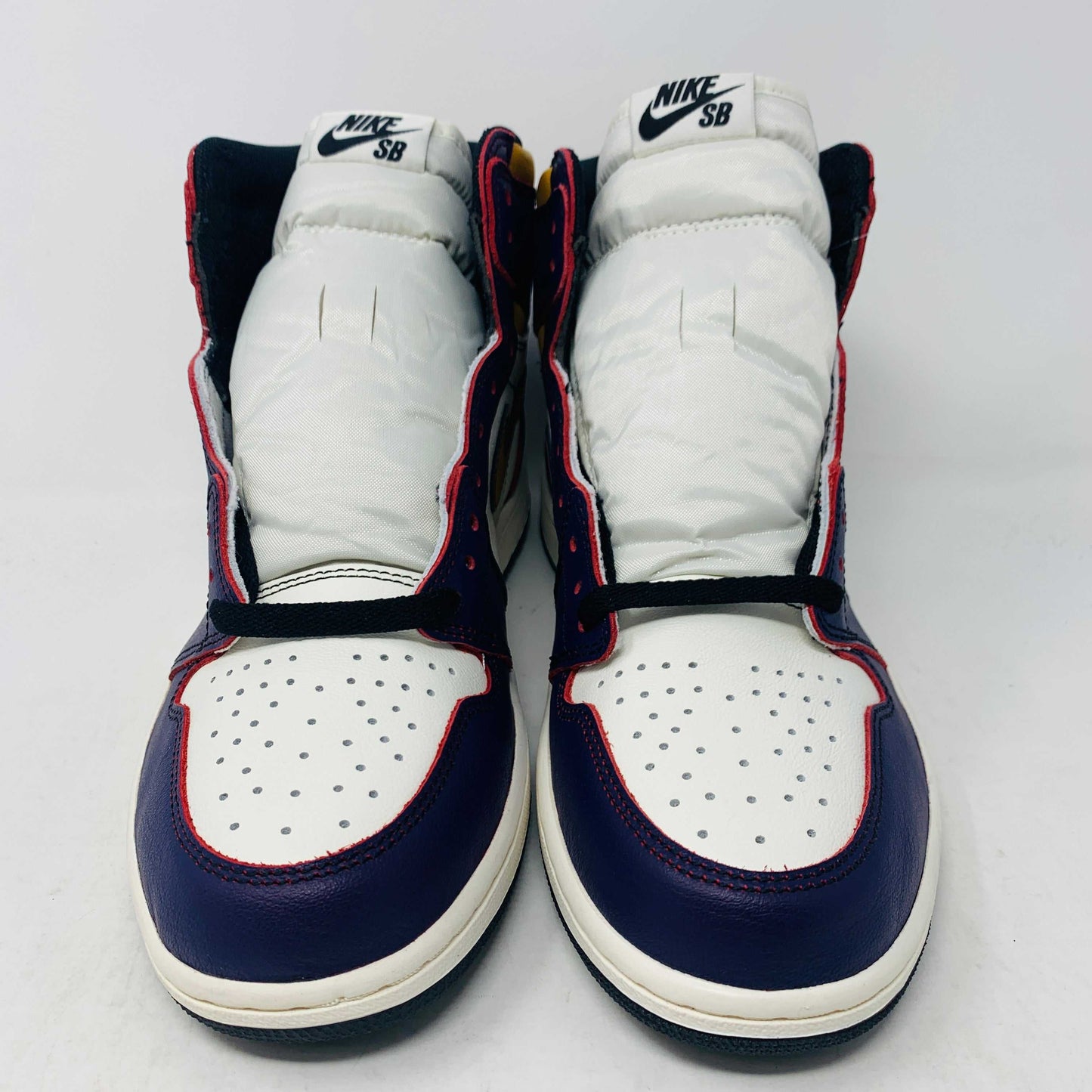 A brand new Jordan 1 High SB LA to Chi sneaker rests on a black Jordan box with a red logo. This authentic high-top shoe features multi-colored accents of purple, yellow, white, and red, with the label proudly reading 1985 Air Jordan 1.