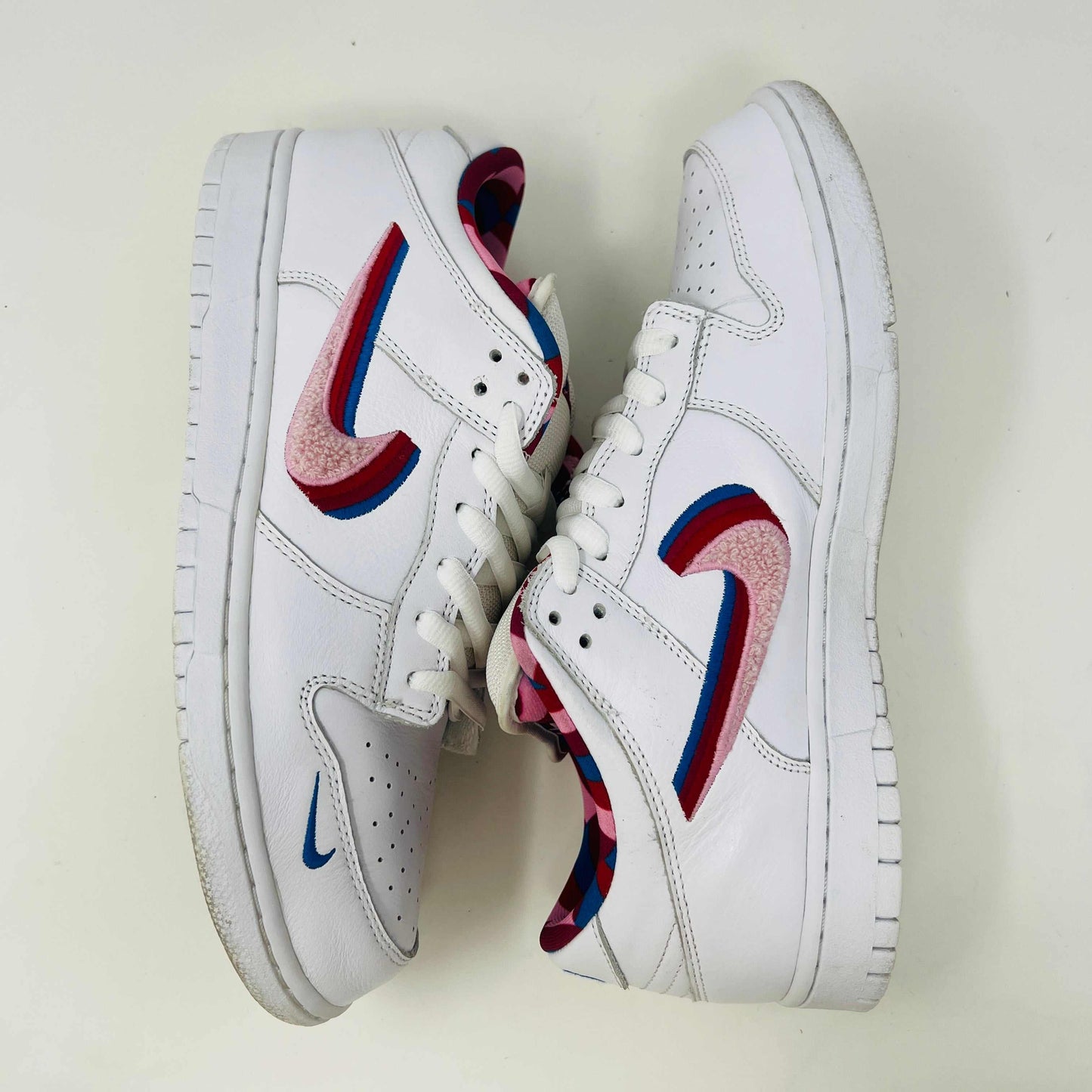 A white Nike SB Dunk Low Parra from 2019 with a multicolored swoosh rests on a black and teal box. The authentic shoes feature clean uppers, size 10.5, as indicated on the label.