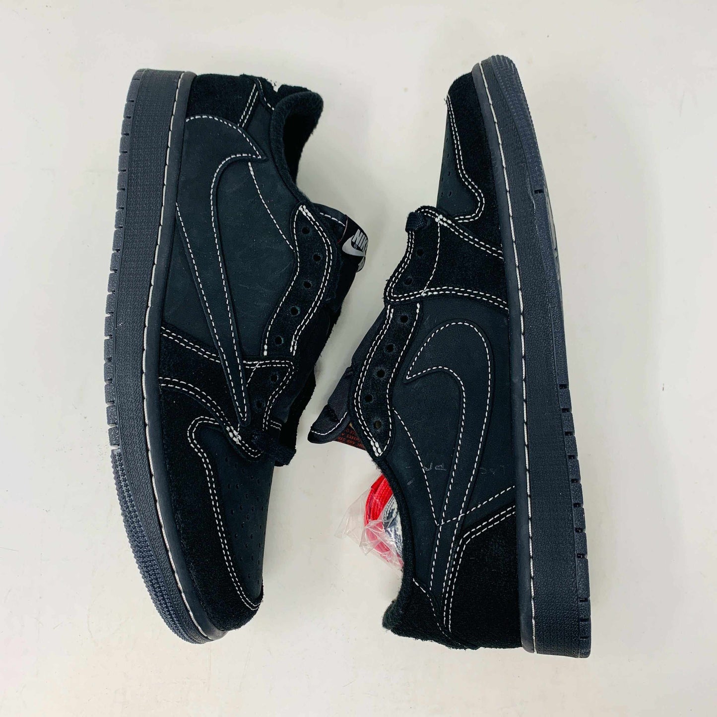 The Jordan 1 Low Travis Phantom sneakers, in black with white stitching, rest on a matching box. Authenticity shines through their design, enhanced by red inserts and the boxs subtle features.