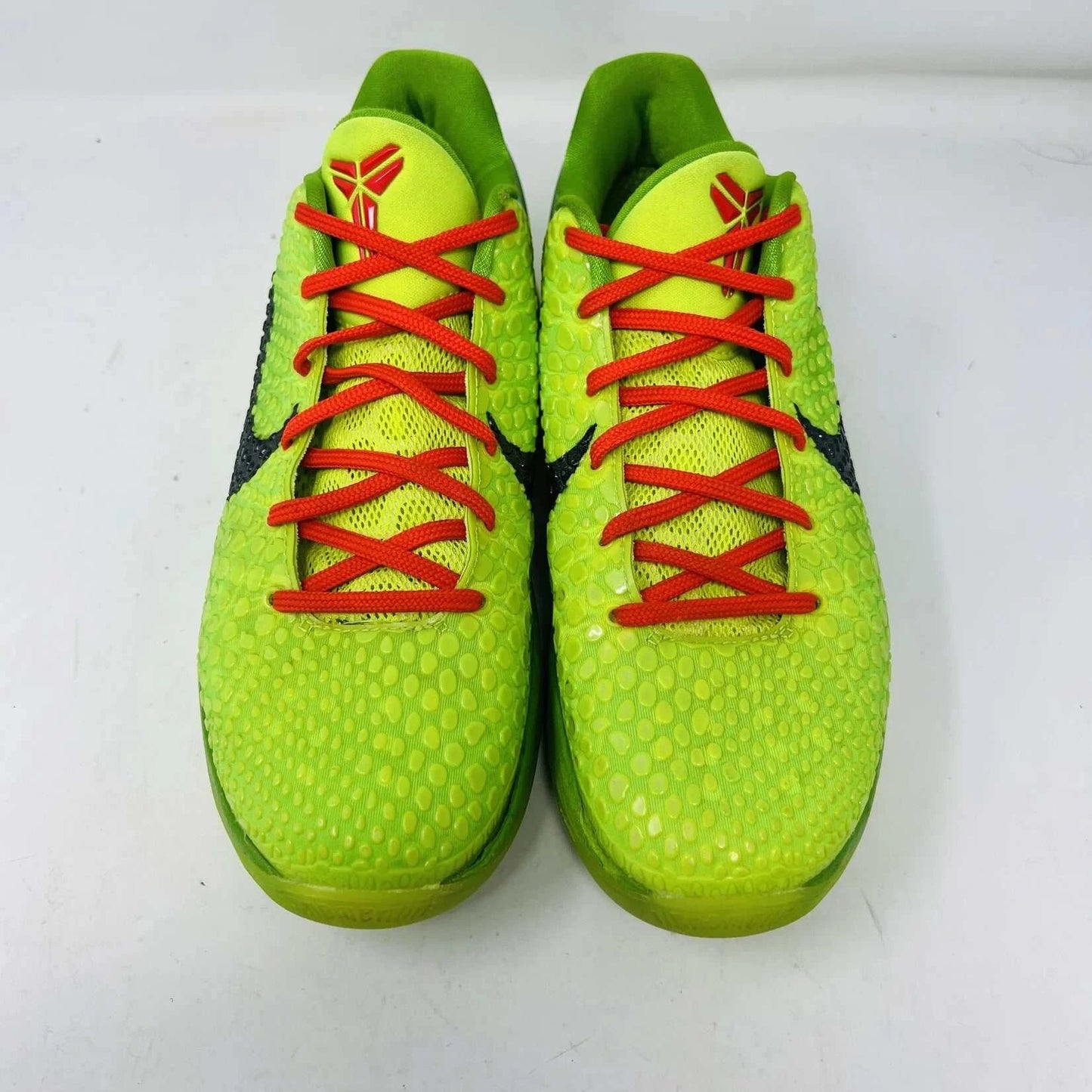 The Nike Kobe 6 Protro Grinch (2020) sports shoes are bright green with a textured surface, red laces, and feature the iconic black Nike swoosh logo. Zoom Air technology is indicated on their side. They are presented against a plain background.