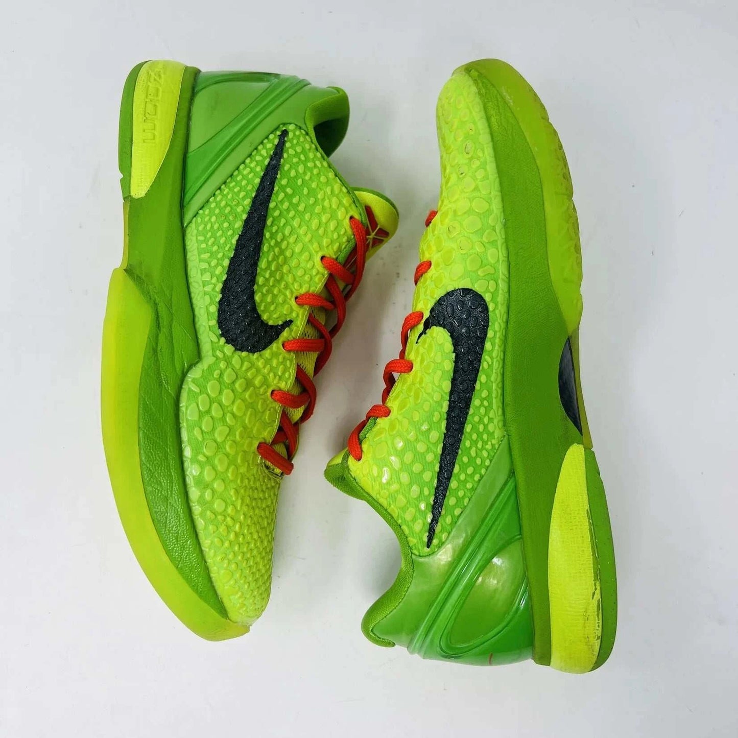 The Nike Kobe 6 Protro Grinch (2020) sports shoes are bright green with a textured surface, red laces, and feature the iconic black Nike swoosh logo. Zoom Air technology is indicated on their side. They are presented against a plain background.