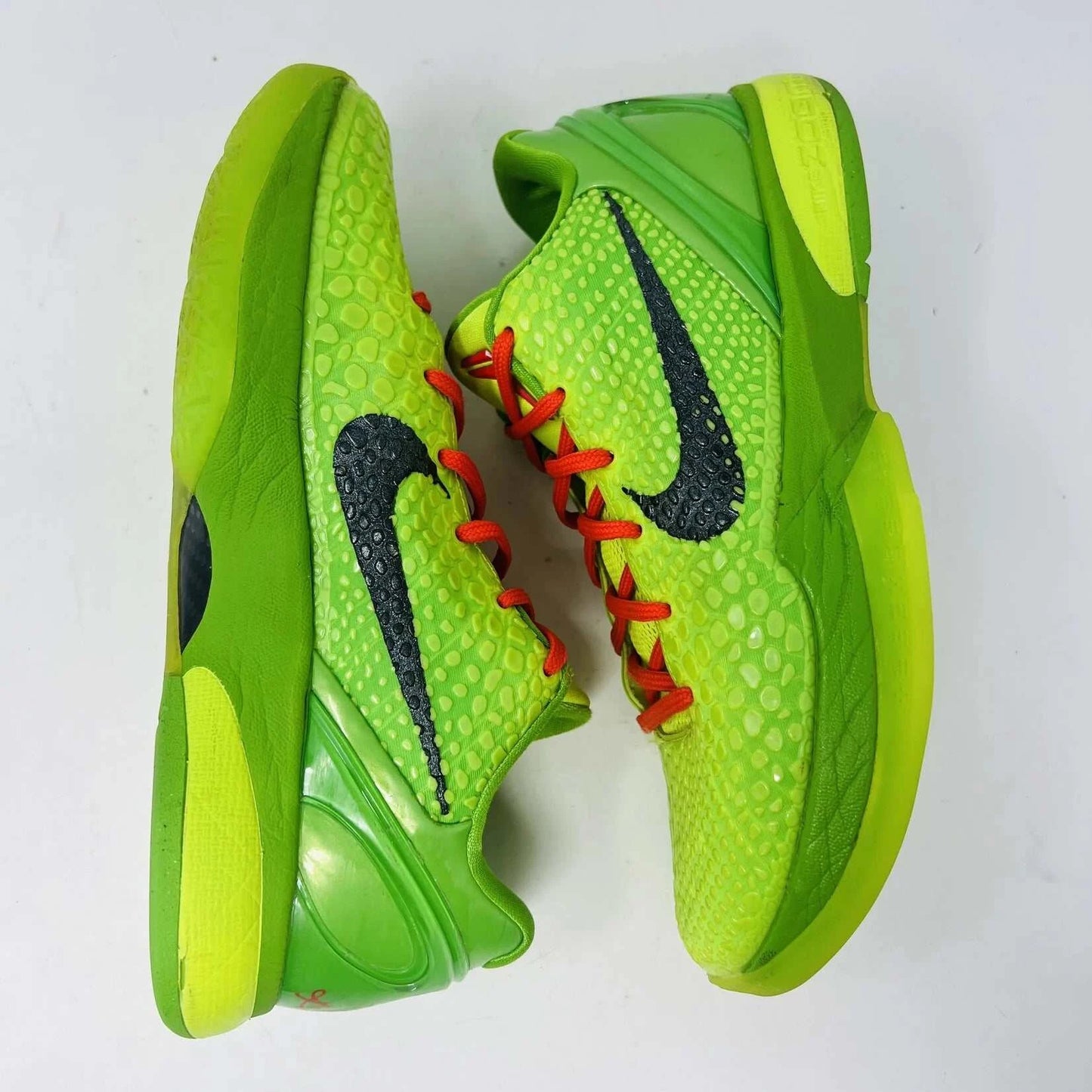 The Nike Kobe 6 Protro Grinch (2020) sports shoes are bright green with a textured surface, red laces, and feature the iconic black Nike swoosh logo. Zoom Air technology is indicated on their side. They are presented against a plain background.