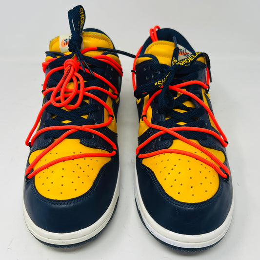 The 2019 Nike Dunk Low Off-White University Gold sneakers feature a navy and yellow design, accented with bold red laces and attached white tags and a zip tie. Displayed atop their box, the label lists them as US size 10.5 and UK size 12, all set against a plain white background.