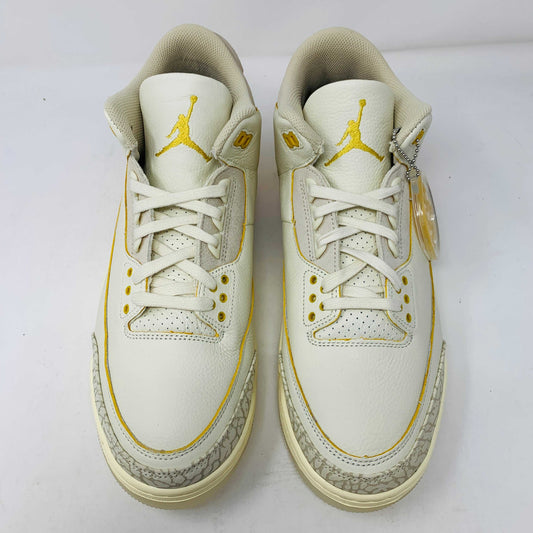The Jordan 3 Retro SP J Balvin Medellín Sunset features a unique design in white and yellow with logo details on the tongue and side, white laces, textured patterns on the sides and soles, and a hanging tag on one shoe.