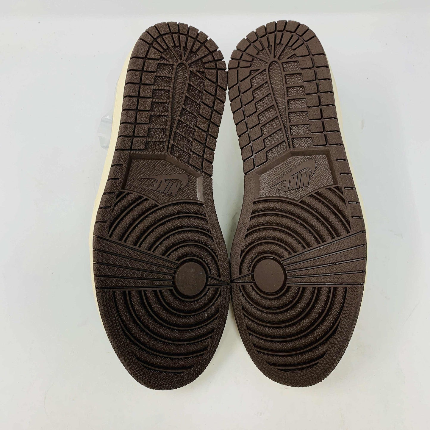 A pair of BRAND NEW Jordan 1 Low OG Travis Scott Mocha sneakers in black and brown, featuring a white swoosh, displayed on a brown shoe box with a red logo. 100% Authentic with EXTRA LACES partially visible inside.