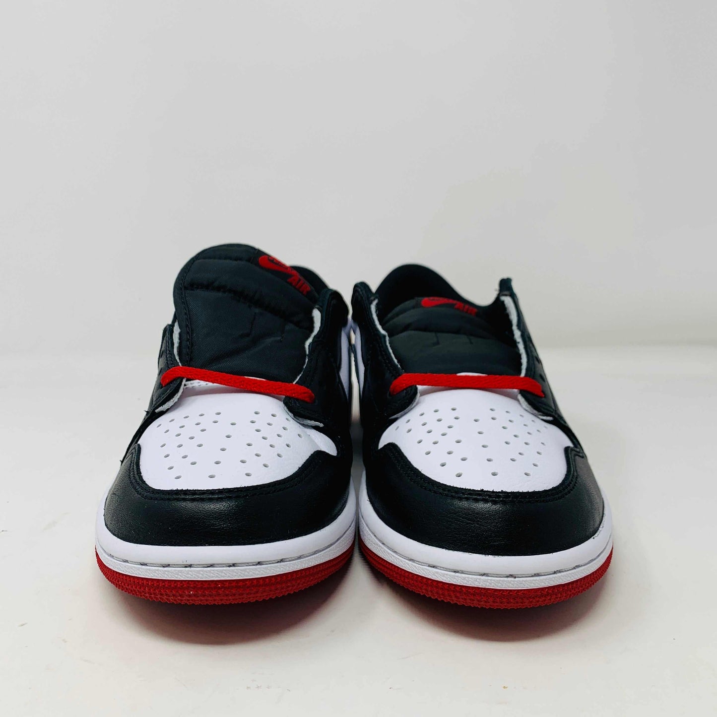 Discover the Jordan 1 Retro Low OG Black Toe (2023) sneakers featuring genuine black and white leather panels, red laces, and soles. These low-tops from Jordan come with extra laces and are displayed on a clean white surface against a pristine background.