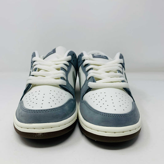 The Nike SB Dunk Low Yuto Horigome sneaker, with a white and light blue design featuring a gray swoosh, is displayed on a white Nike SB box. The authentic shoe has pink and brown laces, a brown sole, and an embroidered logo on the heel.