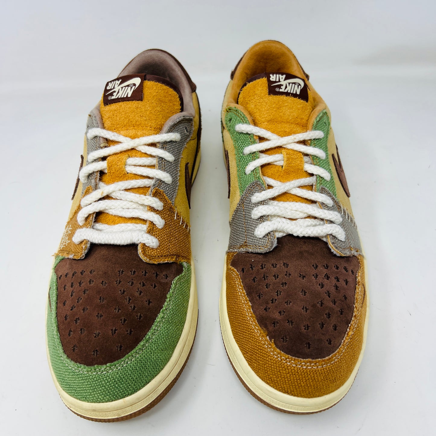 Multicolored Jordan 1 Retro Low OG Zion Williamson Voodoo sneakers feature a patchwork design and visible stitching with brown, yellow, and green sections. The stylish kicks have clean uppers with minimal heel drag, set elegantly on a purple box displaying size and price labels.